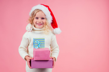 amazed and surprised blonde little girl in red santa hat holding a bunch of gifts boxes and cute...