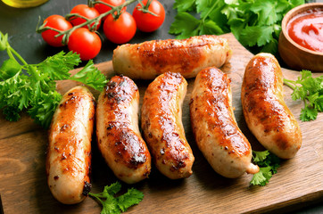 Fried sausages on a cutting board, sause and cherry tomatoes