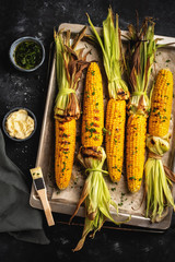 grilled corn on a baking sheet, top view, dark background, rustic style