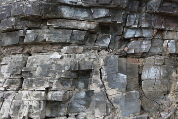 Background on the basis of the texture of rock. Black-gray stone with horizontal layers and cracks