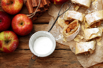 Apple strudel cake with  fresh red apples, sugar powder and cinnamon on rustic wooden table