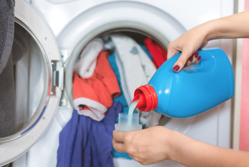 Woman is holding in hands a liquid laundry detergent on a washing machine background.
