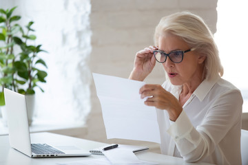 Confused senior businesswoman surprised reading paper letter