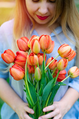 Young pretty caucasian smiling woman is holding a bouquet of red tulips, dating, wedding day, vertical