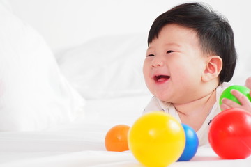 Fototapeta na wymiar Portrait of Asian cute newborn baby playing colorful plastic balls on white bed with happy face and smiling after waking up in the morning. Child playing toys and lovely healthy baby concept