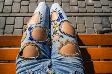 Street fashion, woman in grunge jeans with beads decor is sitting on a bench in city park, top view