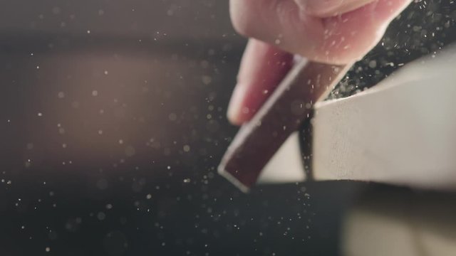 Slow motion woodworker hand sanding walnut board with sand block