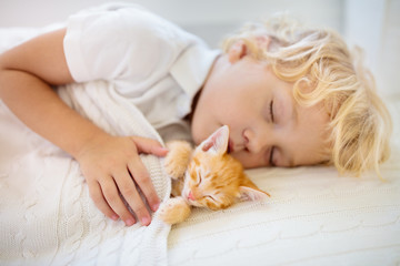 Baby boy sleeping with kitten. Child and cat.