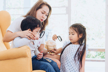 Happy time of family. Mom teaching her son and daugther to used magnifying glass looking on globe at home. Learning and discovery convept.