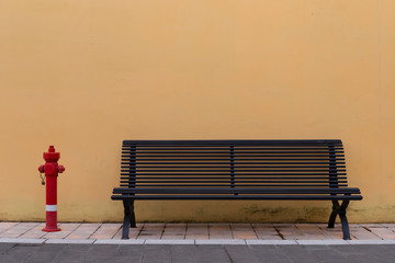 Outdoor bench with hydrant in front of a yellow wall
