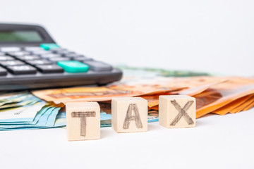 Taxes and spending concept. Tax word writen on wooden cubes. Euro banknotes Laid out in a semicicircle and calculator.Copy space for text. Euro money and calculator on white background.