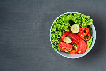 Full bowl of low calories salad with tomato, pepper, cucumber lies on scratched dark concrete. Vegetarian, dieting, healthy food. Space for text. Top view