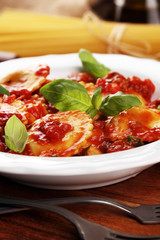 Ravioli with tomato sauce garnished with parmesan cheese and basil on rustic table