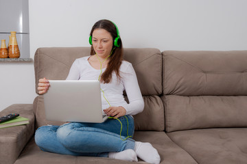 Happy woman using laptop and listening to music on a comfortable sofa.