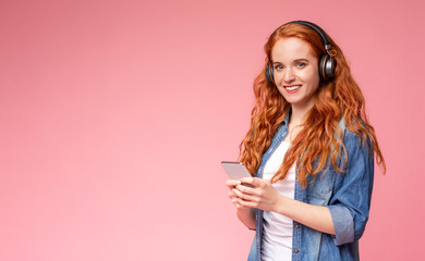 Cheerful girl with red hair listening music online on smartphone