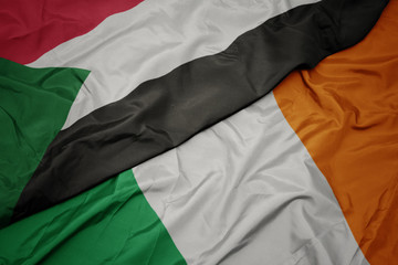 waving colorful flag of ireland and national flag of sudan.