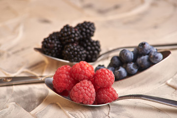 mix of fresh delicious berries lying on spoons and a light background