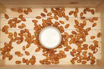 Healthy diet drink almond milk. A glass of white almond milk with almond nuts around in a wooden box. Healthy living concept. Flat lay or top view.