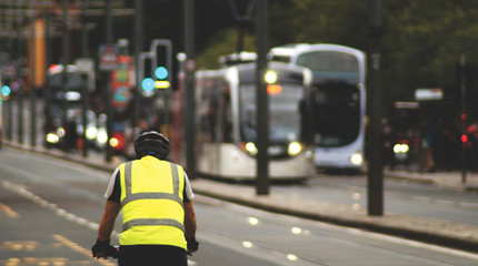 A cyclist wearing a high visibility jacket and a helmet cycling on Princes Street in Edinburgh, Scotland, UK  - obrazy, fototapety, plakaty
