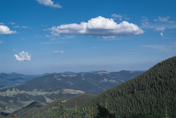 The mountains on a sunny day with clouds and coniferous forest. Landscape