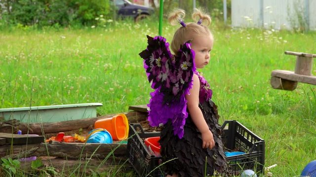 Little cute blond girl with butterfly wings plays near the sandbox