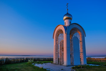 Russia. Western Siberia. Chapel in the rays of sunset on the sea against the blue sky.