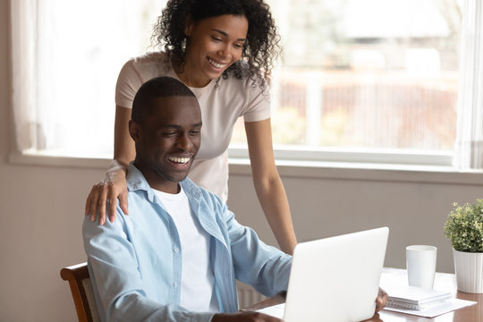 Happy biracial couple look at laptop screen using internet - Powered by Adobe