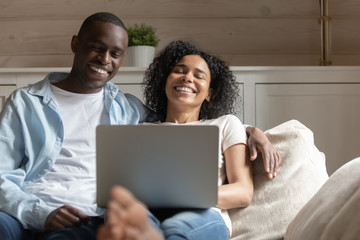 Happy biracial couple relax laugh using laptop at home
