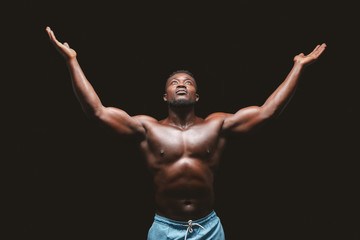 Fototapeta na wymiar Self assured afro bodybuilder raising hands up over black background