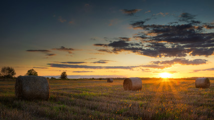 Sun just sets over a field of stubble with haystacks. August countryside landscape...