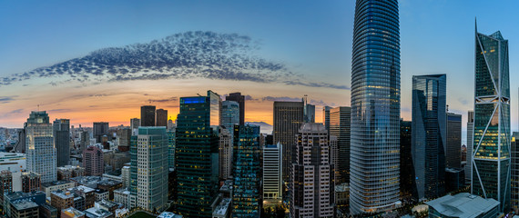 Panorama with light spotted clouds in front of an orange glow of sunset looking over downtown San Francisco