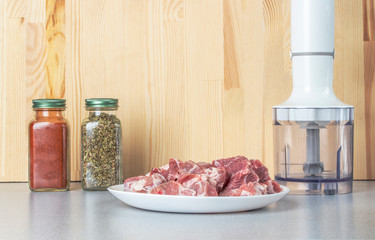 Blender and pieces of meat. Against the background of two glass jars of seasonings.