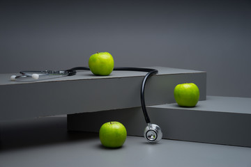 An apple a day keeps the doctor away concept. Stethoscope and green apple concept for diet, healthcare, nutrition or medical insurance on grey based background. 
