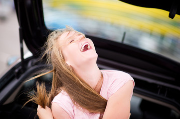 Fototapeta na wymiar girl sits in a car on a summer day and laughs out loud, squinting her eyes