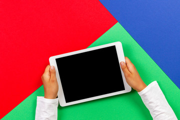 Kid hands holding white tablet computer on light green, blue and red background