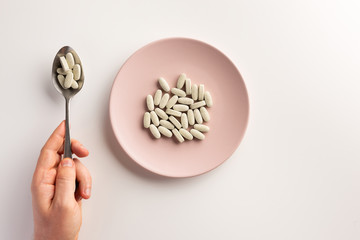 Male hand holding spoon with pills. Plate with pills. Flat lay.