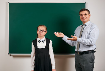 Portrait of a teacher and schoolgirl like as excellent pupil, posing at blackboard background -...