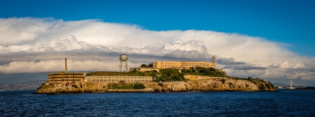 Panorama of Alcatraz Island with grand white clouds behind the old buildings and water tower