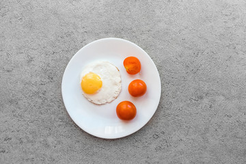 Fried eggs on a white plate with three tomatoes on a gray marble table.