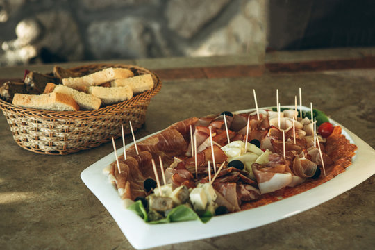 Plate with various meat snacks and cheese. In the background is a plate of bread.