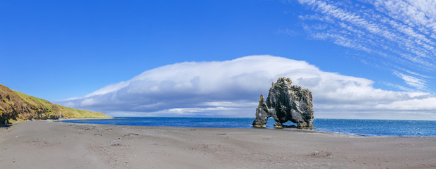Iceland, panoramic view of Hvitserkur sophisticated rock in the sea during low tide at white baroque clouds in background. Icelandic landscape, sunny day scenery.