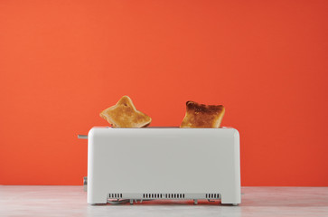 Roasted toast bread popping up of toaster with red wall, front view