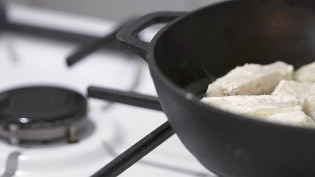Making pan fried cod fish fillet in cast iron frying pan with cooking oil on gas stove.