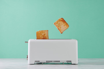Roasted toast bread popping up of toaster with green wall, front view