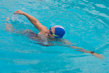 Senior caucasian woman in activity swimming in freestyle stroke. Pratice sport in the swimming pool. Outdoor under the sunlight. With swimming cap and goggles. Healthy lifestyle