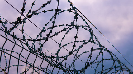 The fence of the correctional facility with barbed wire on the background of a gloomy cloudy dark blue sky.