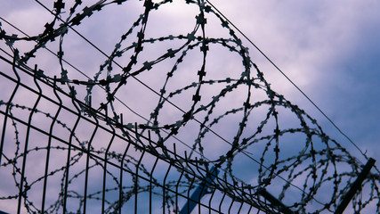 The fence of the correctional facility with barbed wire on the background of a gloomy cloudy dark...
