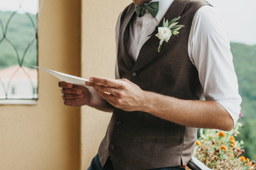 Close-up of a groom holding a sheet of paper in his hands with an oath or invitation. Preparing for...