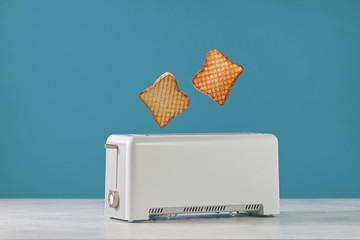 Roasted toast bread popping up of toaster with blue wall, front view