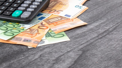 Calculator and euro money on grey wooden desk. Euro banknotes with black calculator on wooden background. Copy space for text. Finances and budget concept.